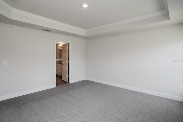 spare room with dark carpet, ornamental molding, and a raised ceiling