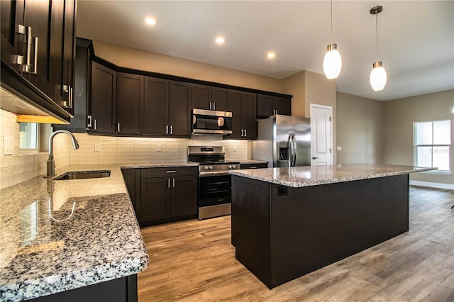 kitchen featuring a center island, sink, hanging light fixtures, light stone countertops, and stainless steel appliances