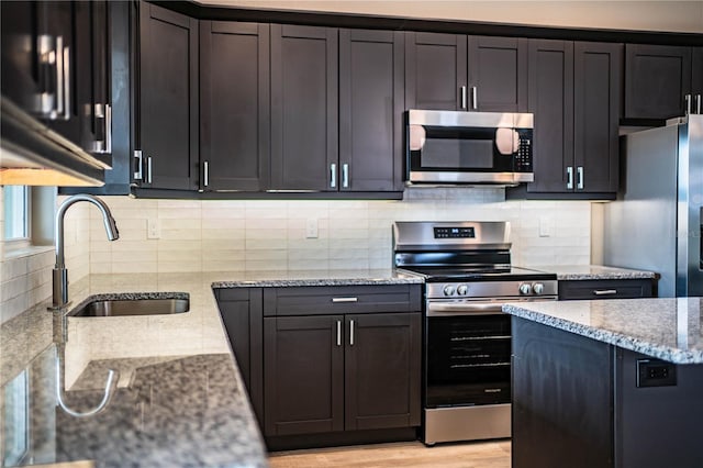 kitchen featuring backsplash, sink, light stone countertops, appliances with stainless steel finishes, and light hardwood / wood-style floors