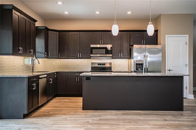 kitchen with light stone countertops, stainless steel appliances, sink, pendant lighting, and a center island