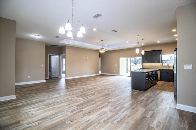 kitchen with a center island, sink, a tray ceiling, ceiling fan with notable chandelier, and hardwood / wood-style flooring