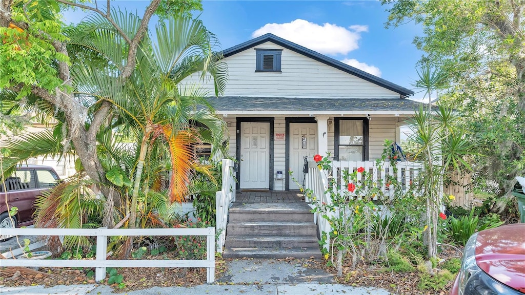 bungalow with roof with shingles, a porch, and a fenced front yard