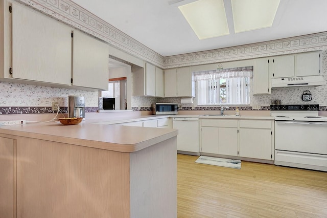 kitchen with kitchen peninsula, a wealth of natural light, white appliances, and light wood-type flooring