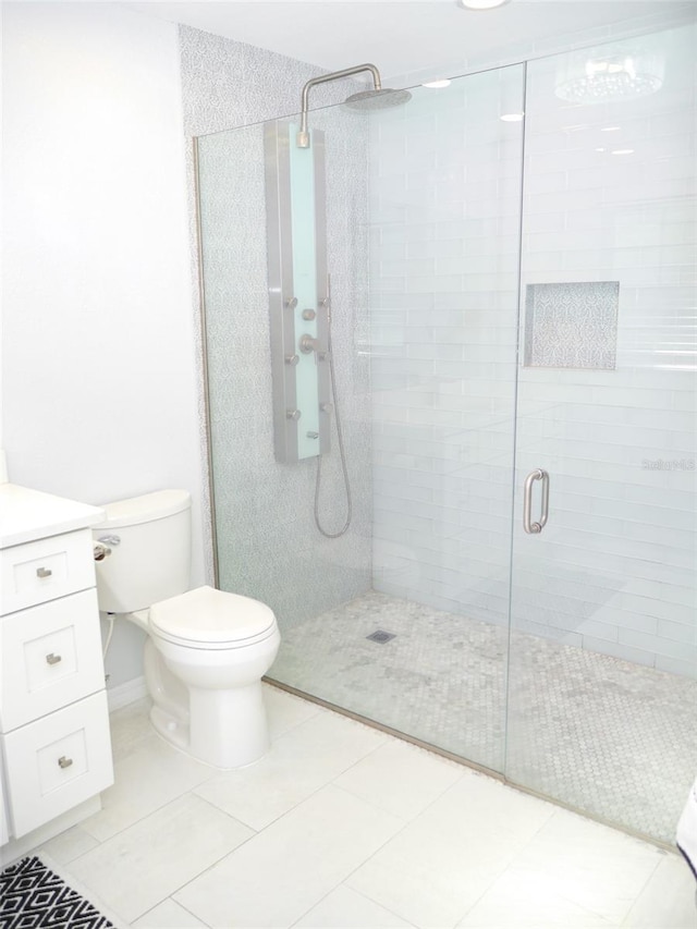 bathroom featuring toilet, vanity, a shower with shower door, and tile patterned floors