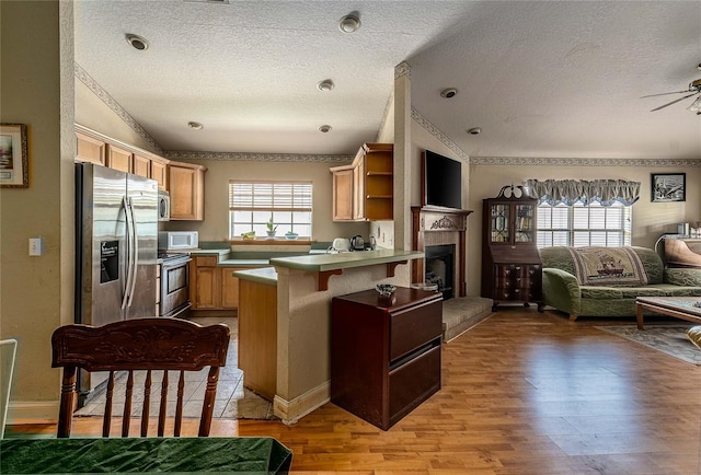 kitchen featuring a textured ceiling, light wood-type flooring, appliances with stainless steel finishes, kitchen peninsula, and ceiling fan