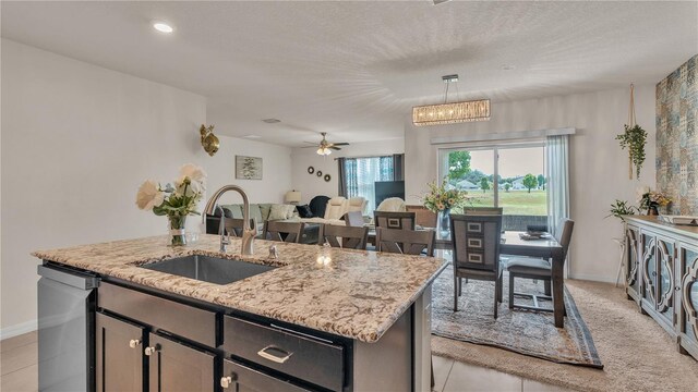 kitchen featuring an island with sink, dishwashing machine, decorative light fixtures, ceiling fan with notable chandelier, and sink