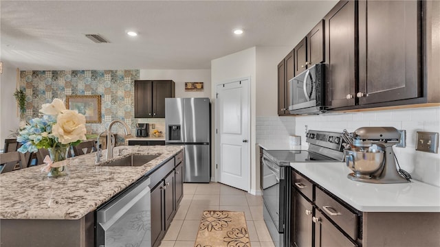 kitchen featuring stainless steel appliances, an island with sink, sink, tasteful backsplash, and light tile floors