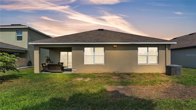 back house at dusk with an outdoor hangout area, a patio area, central air condition unit, and a lawn