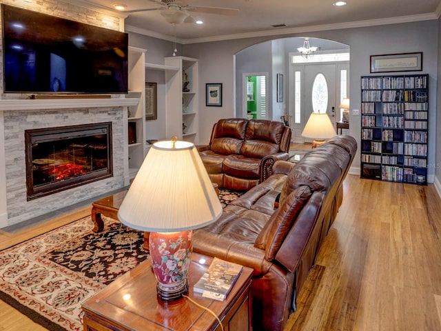 living room with light wood-type flooring, ceiling fan, a fireplace, and crown molding