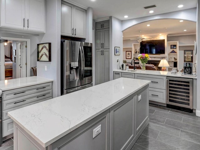 kitchen with a center island, stainless steel fridge with ice dispenser, light stone counters, beverage cooler, and dark tile flooring