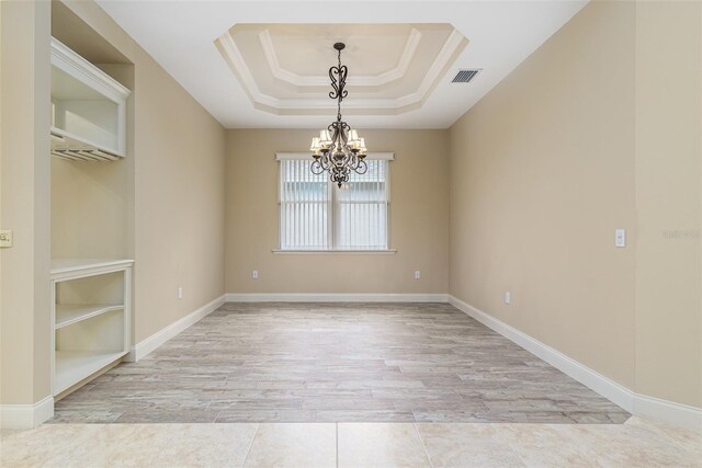 spare room featuring a raised ceiling, light wood-type flooring, crown molding, and a chandelier