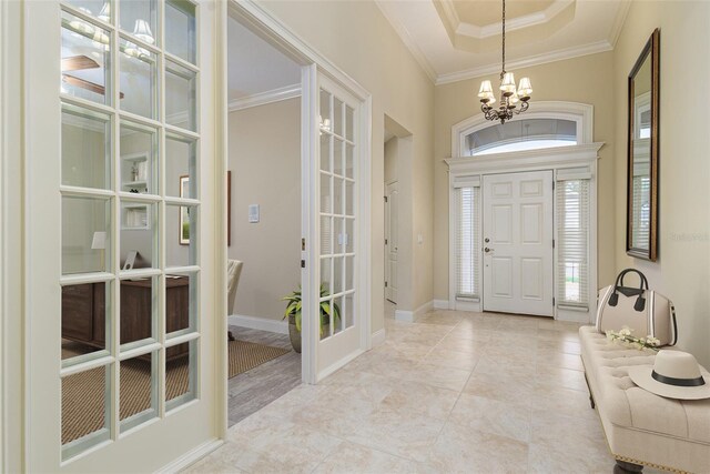 tiled foyer with a raised ceiling, french doors, crown molding, and a chandelier