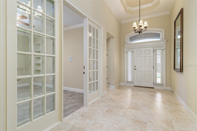 tiled foyer with a notable chandelier, ornamental molding, french doors, and a tray ceiling