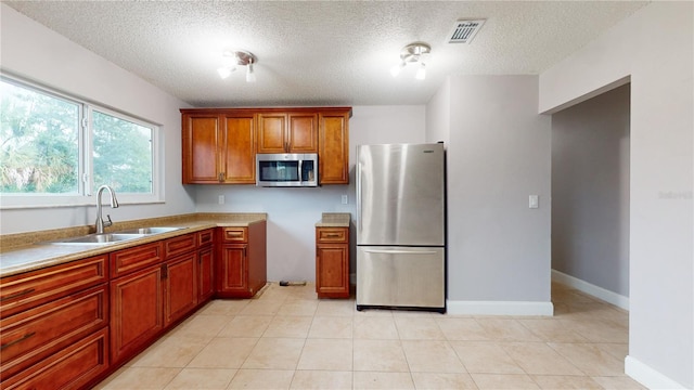 kitchen with stainless steel appliances, sink, a textured ceiling, and light tile floors