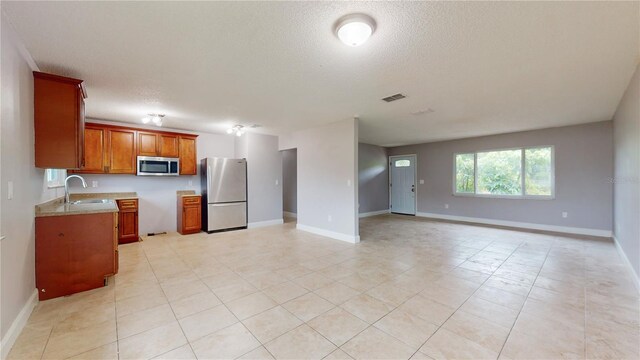 kitchen with appliances with stainless steel finishes, sink, light tile flooring, and a textured ceiling