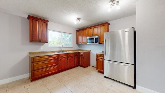 kitchen with a textured ceiling, sink, light tile floors, and appliances with stainless steel finishes