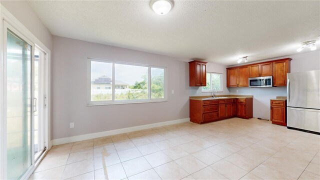 kitchen with appliances with stainless steel finishes, sink, a textured ceiling, and light tile floors