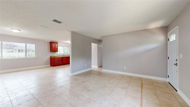 unfurnished living room with sink, a textured ceiling, and light tile floors