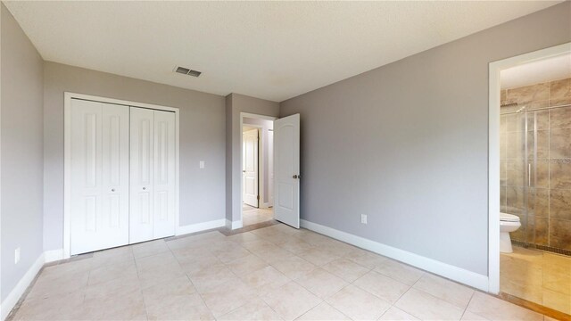 unfurnished bedroom with connected bathroom, a closet, and light tile floors