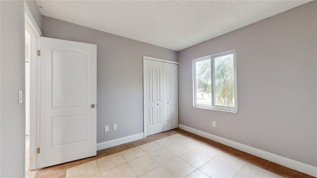 unfurnished bedroom with a closet, light tile flooring, and a textured ceiling