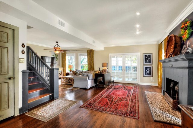 entrance foyer featuring dark hardwood / wood-style flooring, a tiled fireplace, ceiling fan, crown molding, and french doors