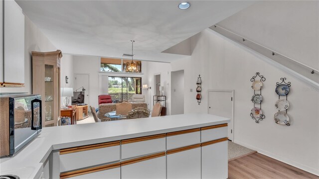 kitchen featuring white cabinets, hanging light fixtures, a notable chandelier, kitchen peninsula, and light hardwood / wood-style flooring