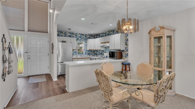 kitchen featuring stainless steel refrigerator, tasteful backsplash, a notable chandelier, white cabinets, and kitchen peninsula