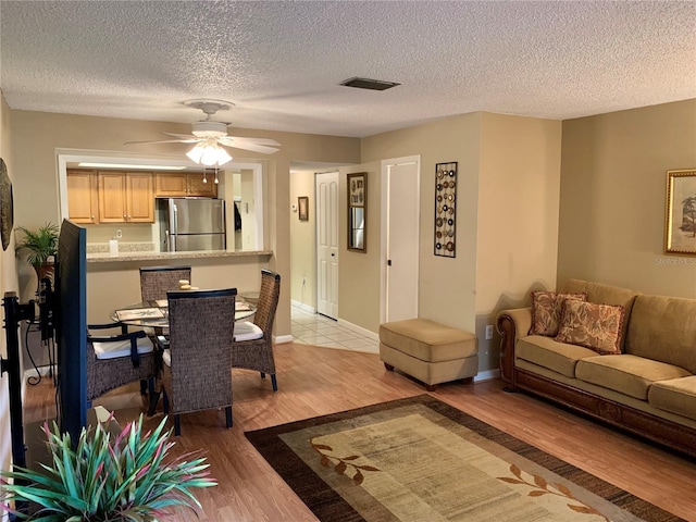 living room with ceiling fan, a textured ceiling, and light wood-type flooring