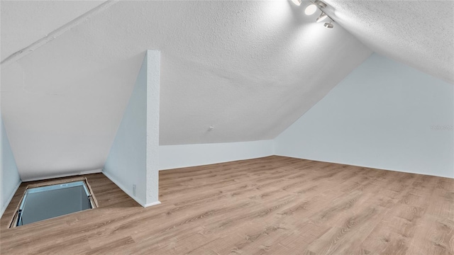 bonus room with vaulted ceiling, light hardwood / wood-style floors, and a textured ceiling