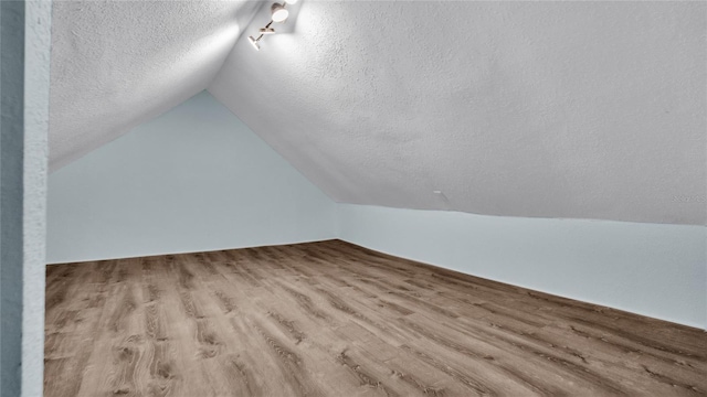 additional living space with lofted ceiling, a textured ceiling, and light hardwood / wood-style flooring