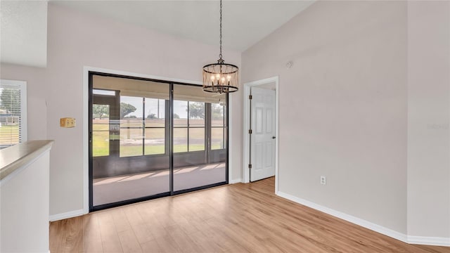 unfurnished dining area featuring lofted ceiling, a healthy amount of sunlight, light wood-type flooring, and a chandelier