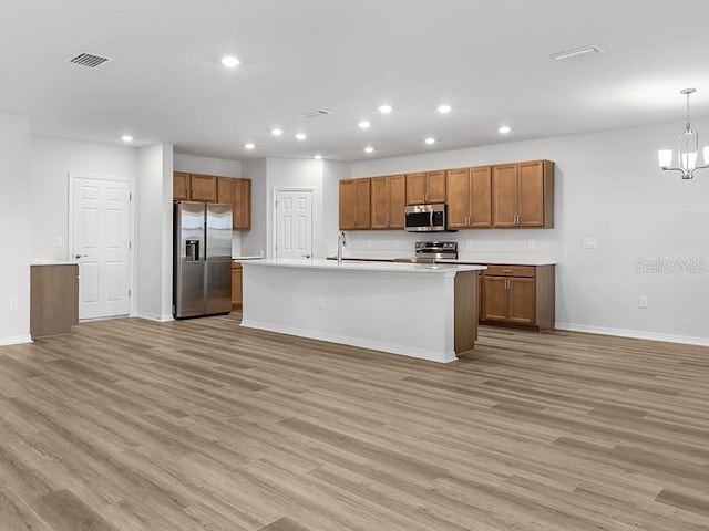 kitchen featuring a kitchen island with sink, sink, stainless steel appliances, and light wood-type flooring