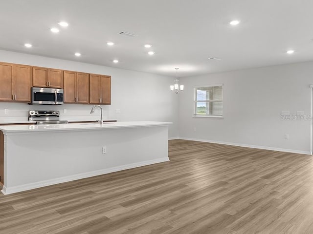 kitchen featuring stainless steel appliances, a kitchen island with sink, sink, pendant lighting, and light hardwood / wood-style flooring