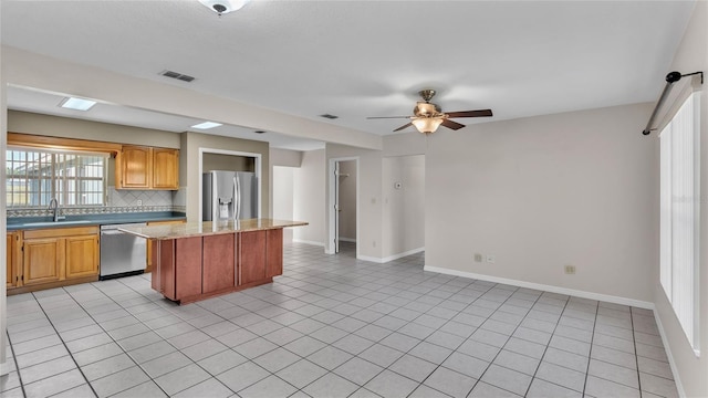 kitchen with ceiling fan, a center island, backsplash, light tile patterned floors, and appliances with stainless steel finishes