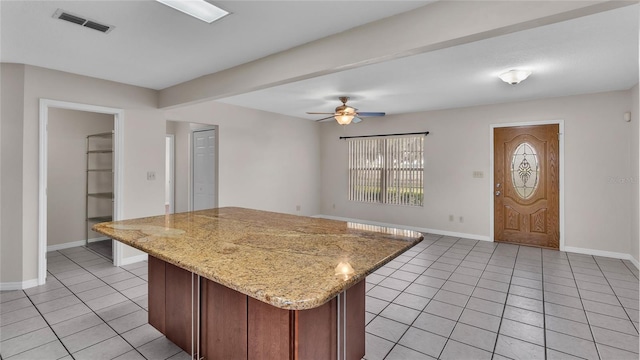 kitchen with ceiling fan, a kitchen island, light stone counters, and light tile patterned floors