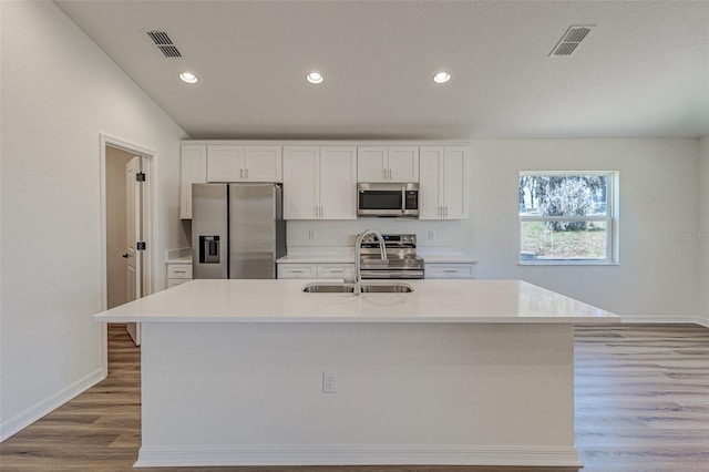 kitchen with appliances with stainless steel finishes, light wood-type flooring, a kitchen island with sink, sink, and white cabinets