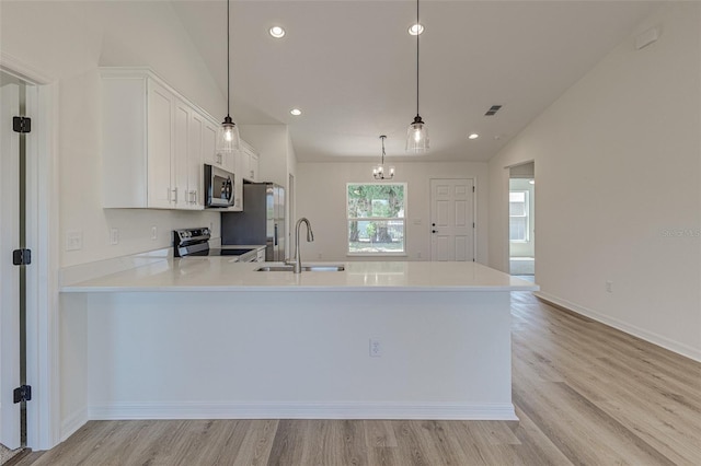 kitchen featuring kitchen peninsula, vaulted ceiling, decorative light fixtures, white cabinets, and appliances with stainless steel finishes