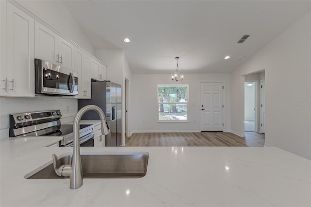 kitchen featuring pendant lighting, lofted ceiling, appliances with stainless steel finishes, light hardwood / wood-style floors, and light stone counters