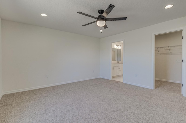 unfurnished bedroom featuring ensuite bath, ceiling fan, a spacious closet, light colored carpet, and a closet