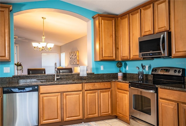 kitchen with sink, a chandelier, dark stone counters, pendant lighting, and stainless steel appliances