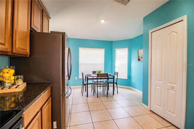 kitchen featuring light tile patterned floors, electric range oven, dark stone counters, and stainless steel refrigerator