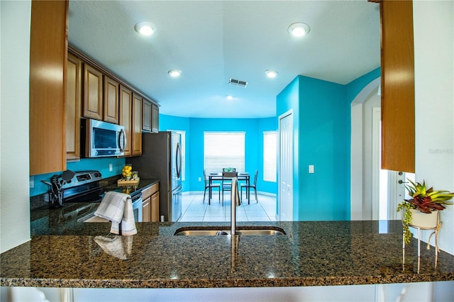 kitchen featuring stainless steel appliances, sink, kitchen peninsula, and dark stone counters