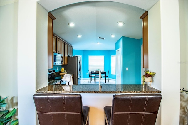 kitchen featuring appliances with stainless steel finishes, dark stone countertops, and kitchen peninsula