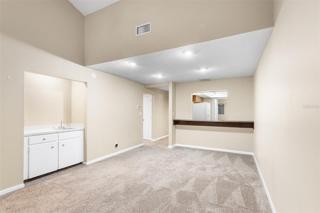 spare room featuring light colored carpet, sink, a textured ceiling, and a high ceiling