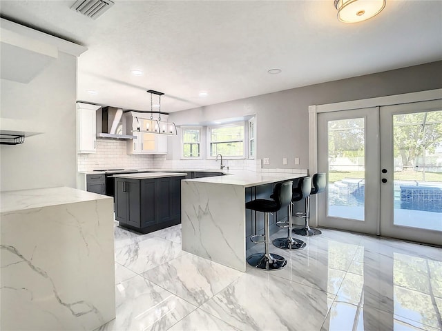 kitchen featuring pendant lighting, white cabinets, kitchen peninsula, light stone countertops, and wall chimney range hood