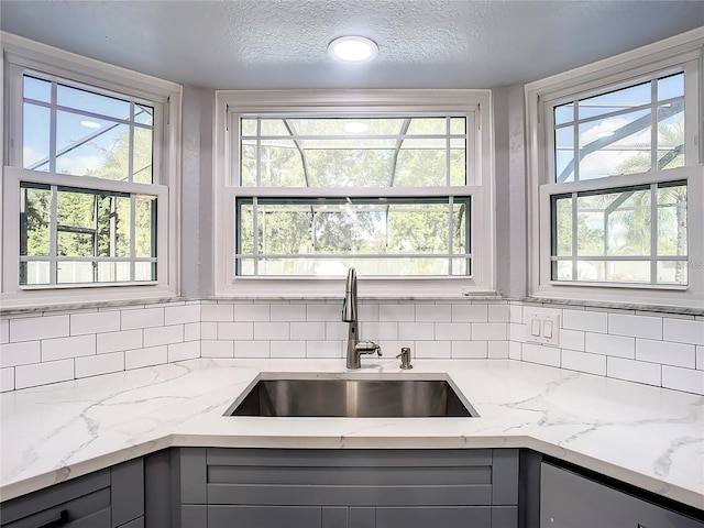 kitchen featuring gray cabinetry, sink, light stone counters, and a textured ceiling