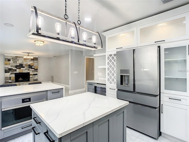 kitchen with light stone countertops, gray cabinets, stainless steel appliances, and a kitchen island