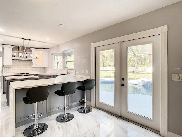 kitchen featuring pendant lighting, white cabinetry, sink, a kitchen breakfast bar, and french doors
