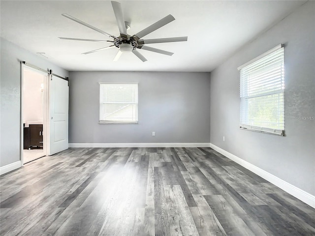unfurnished bedroom featuring wood-type flooring, a barn door, ensuite bathroom, and ceiling fan