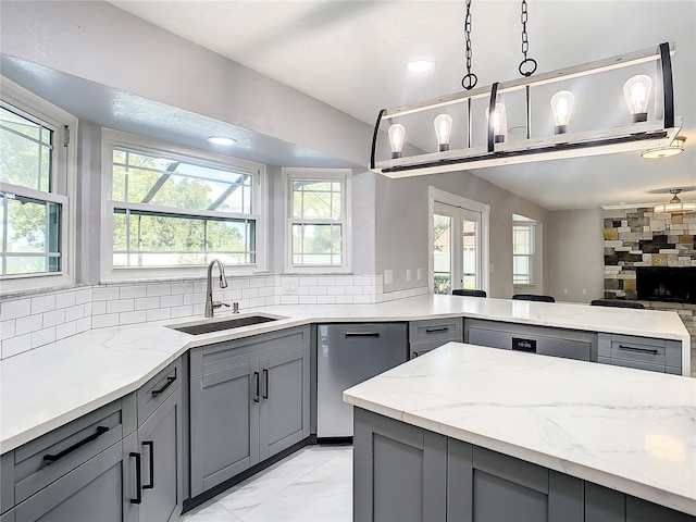 kitchen with sink, dishwasher, gray cabinetry, hanging light fixtures, and light stone countertops